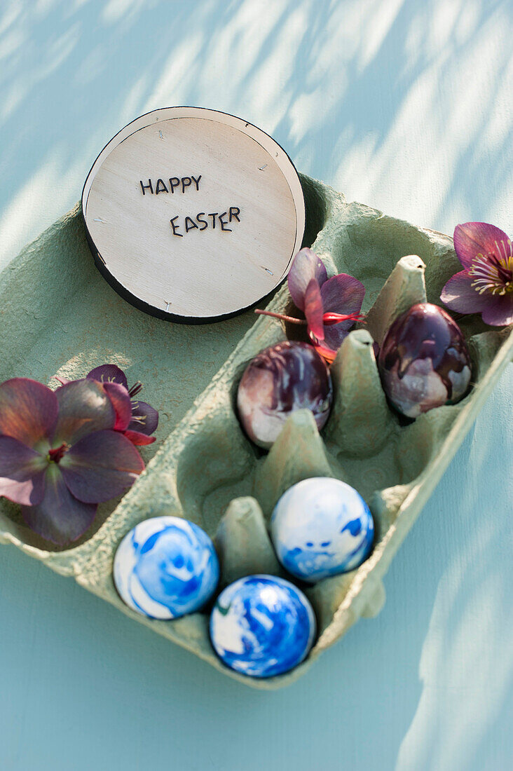 Eierkarton mit Frühlingsblüten, Ostereiern und Botschaft in Holzkiste