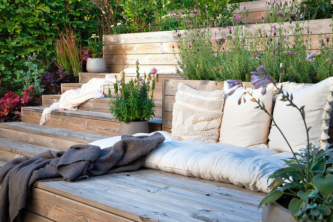 Seating area on wooden terrace with cushions and plants in the background