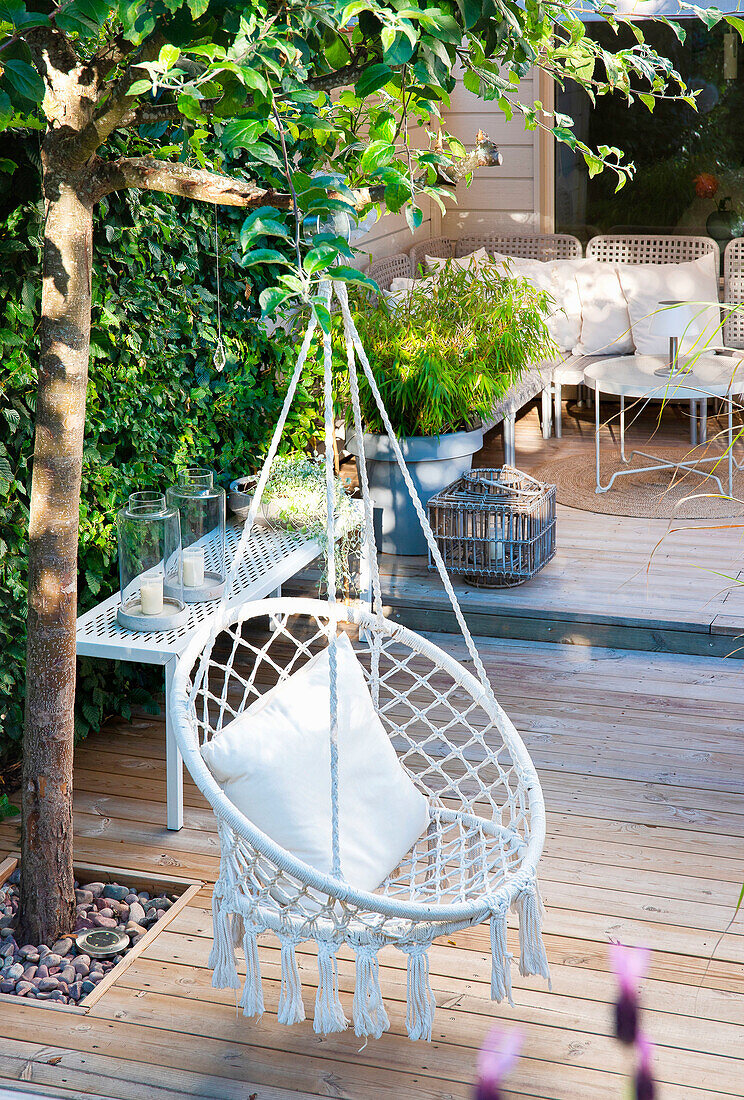 Hanging chair made of rattan with cushions on a wooden terrace in the countryside