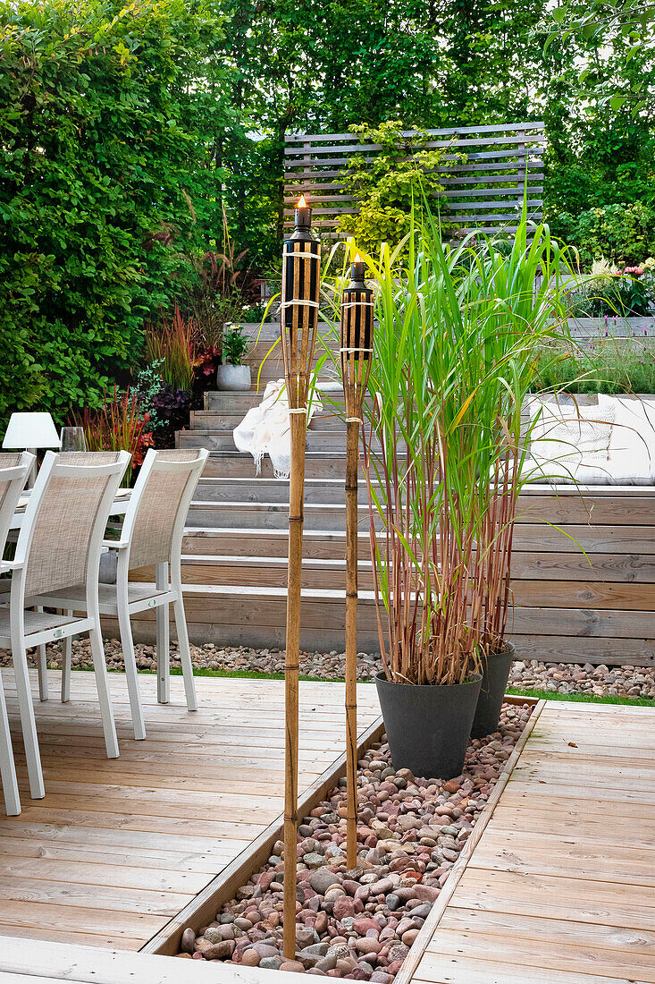 Terrasse mit Holzdielen, Fackeln und Pflanzkübel mit Schilf