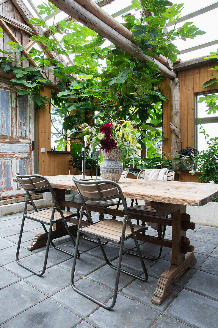 Wooden table with chairs on recycled tiled floor in a renovated barn with a glass roof