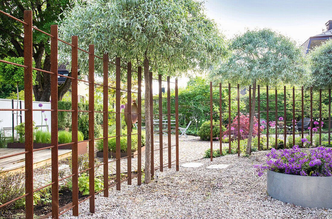 Flowerbed surrounded by gravel and metal trellis with stainless steel raised bed