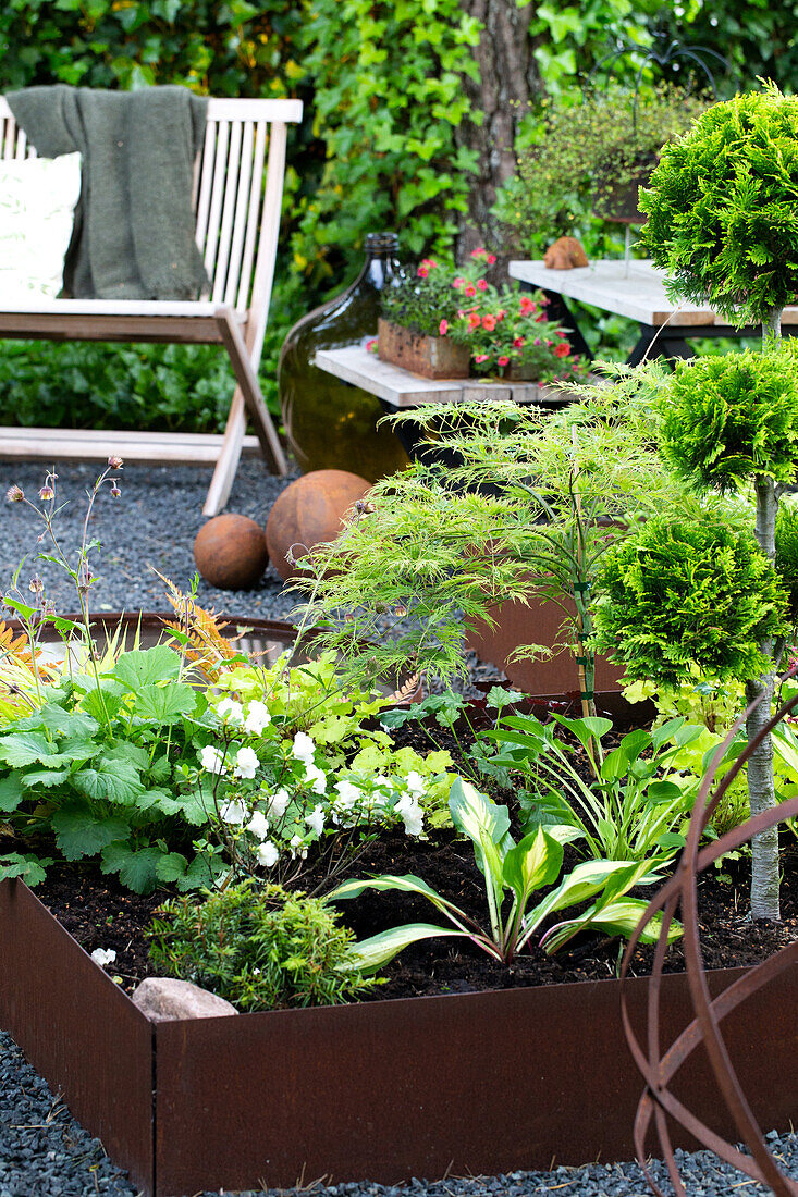 Raised bed and decorative ball made of Corten steel, wooden bench in the background