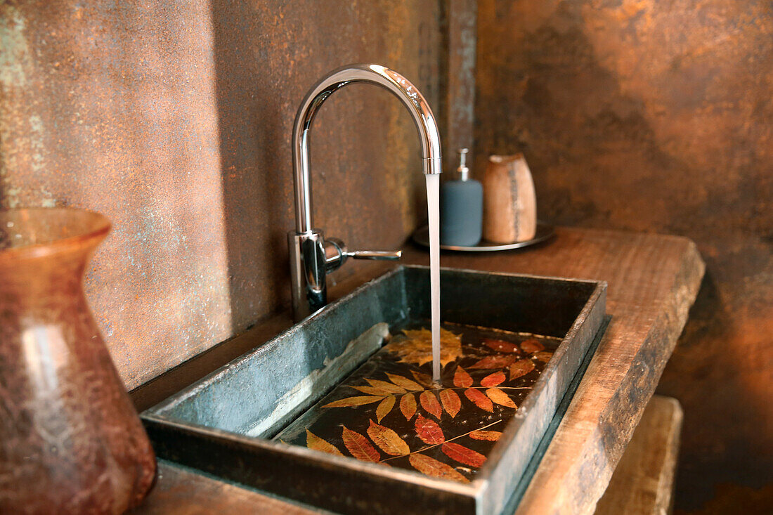 Waschbecken und Wasserhahn aus Edelstahl im Badezimmer mit Wandverkleidung aus Cortenstahl