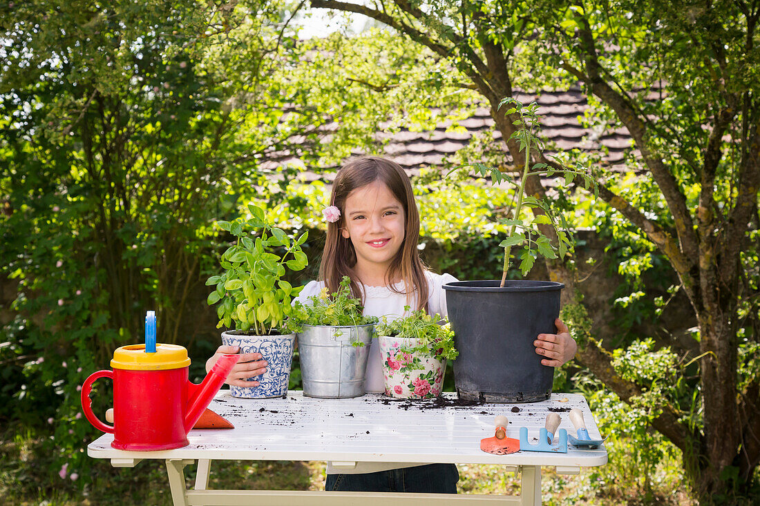 Portrait of proud little girl with potted spice plants on table in the garden