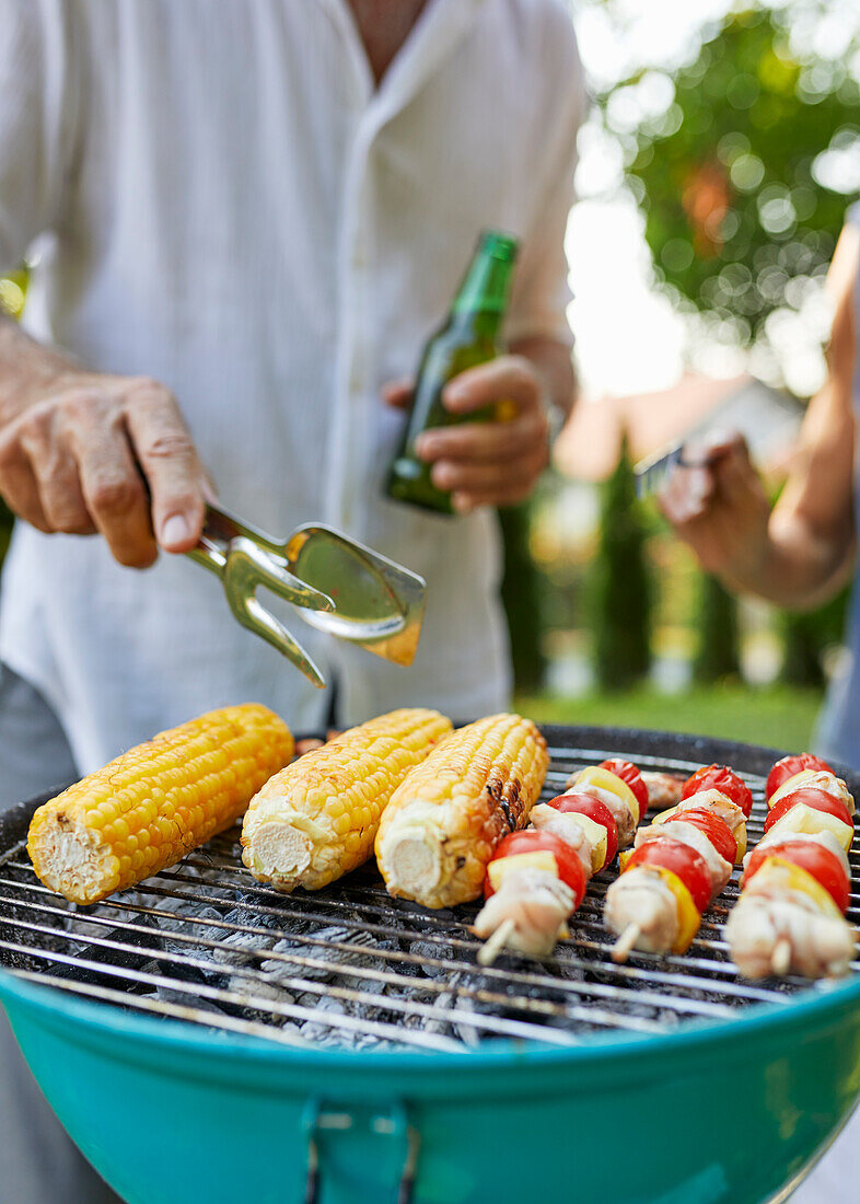 Corn cob and meat skewer on grill at barbecue in garden