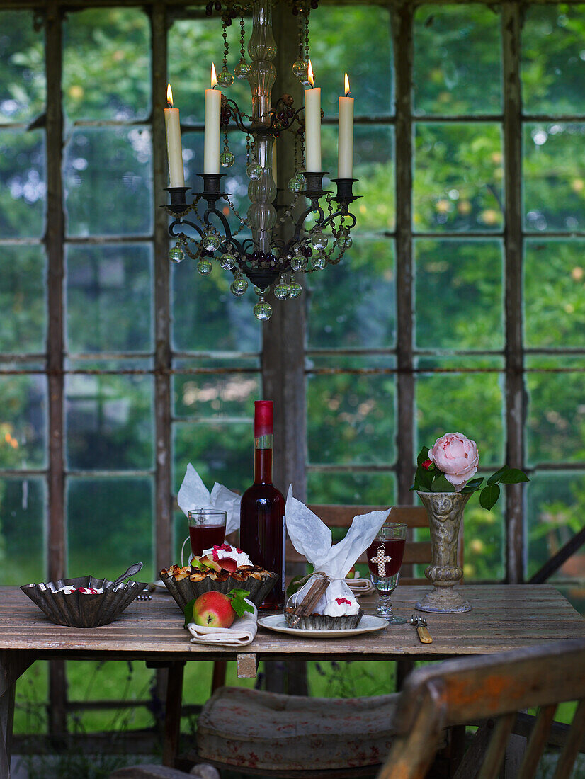 Alter Holztisch mit Kuchen und Beerensaft, darüber Kerzenleuchter im Wintergarten