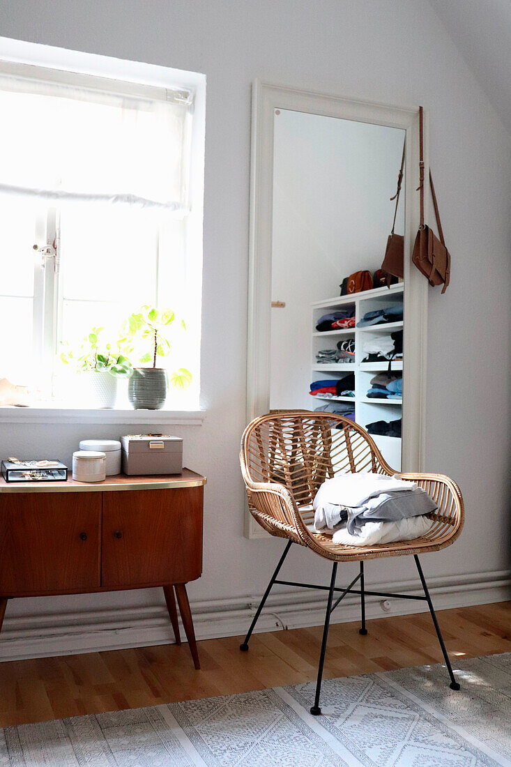 Modern rattan chair and vintage wooden chest of drawers in light-coloured dressing room