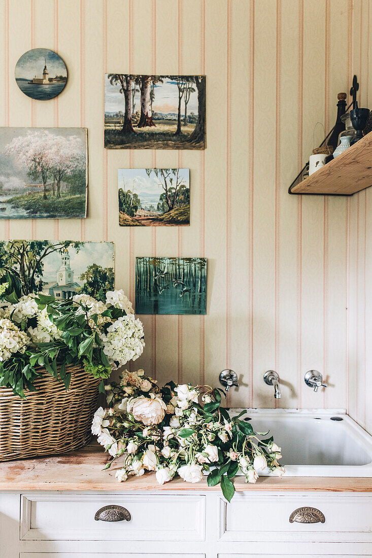 Sammlung alter Gemälde über Waschbecken im Waschraum, Korb mit Blumen