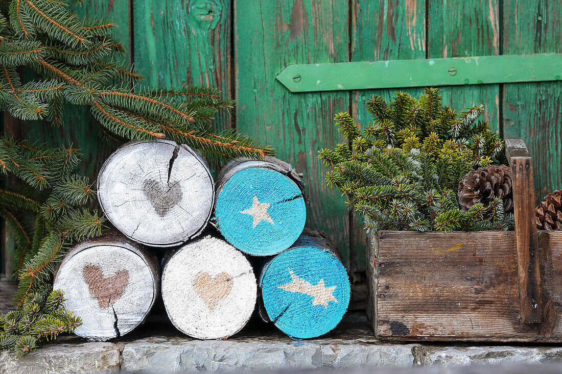 Holzstämme mit Weihnachtsmotiven, Nadelzweige und Zapfen in Holzkiste
