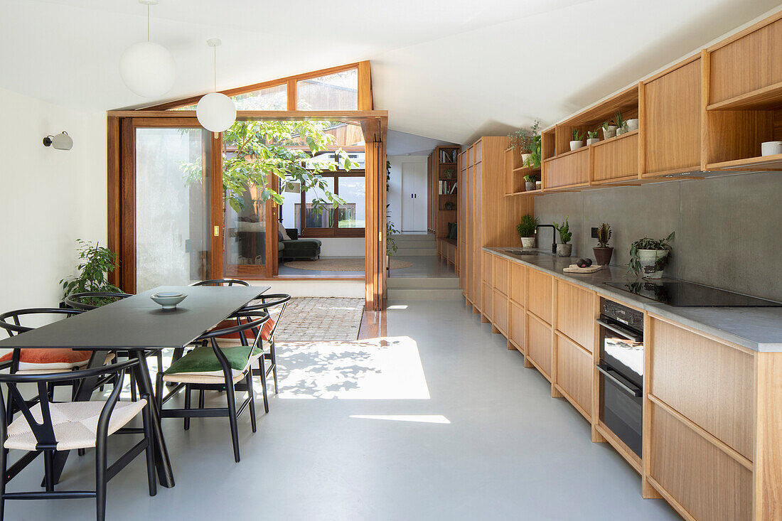 Fitted kitchen with wooden fronts and dining area; view of tree planted in atrium