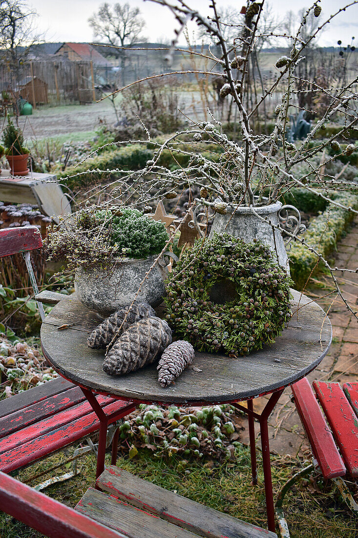Steintöpfe, Lärchenzweige und Lebensbaumkranz auf Gartentisch