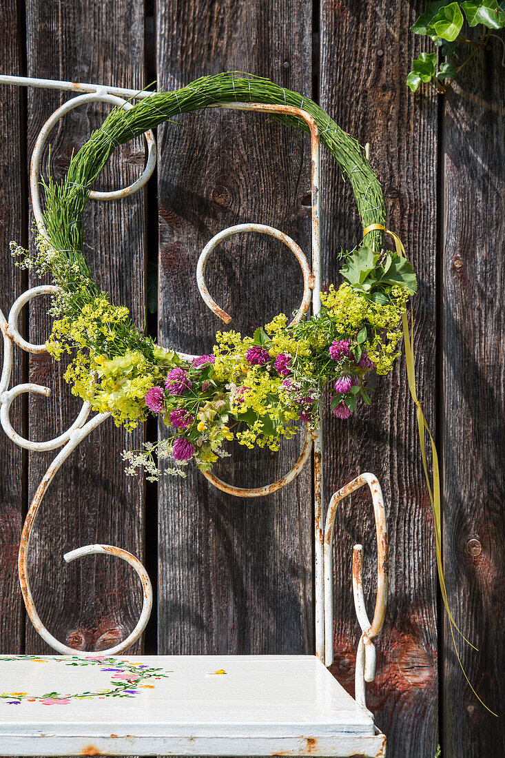 Kranz aus frischen Blumen an Gartenbank vor rustikaler Holzwand