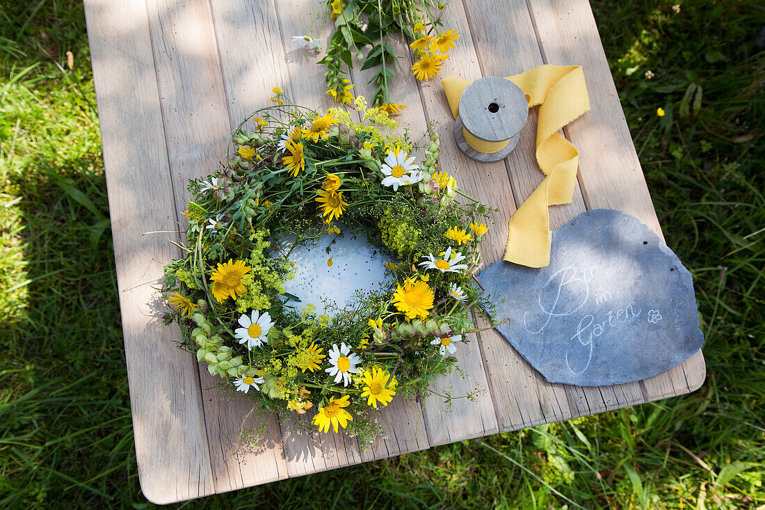 Summery flower wreath on wooden table next to slate sign with inscription Am in the garden