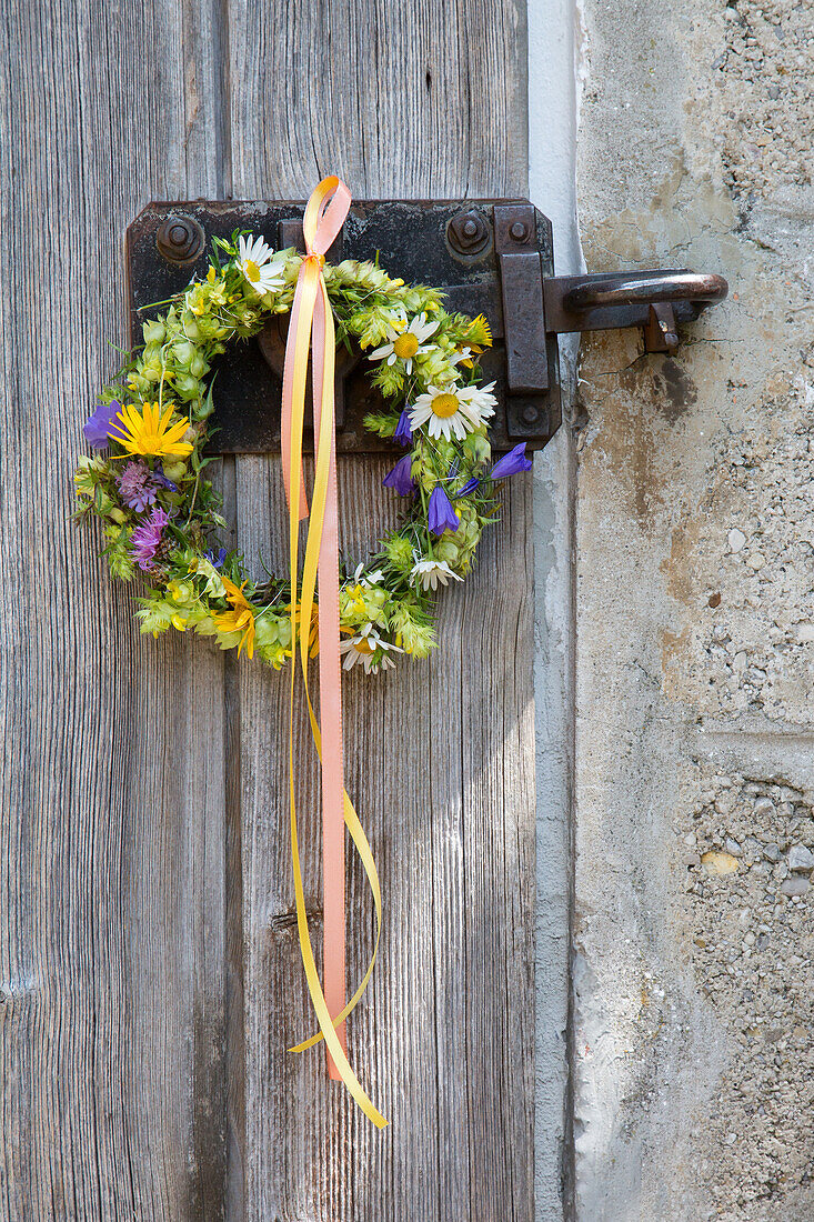 Wreath of flowers attached to an old wooden door with colourful ribbons