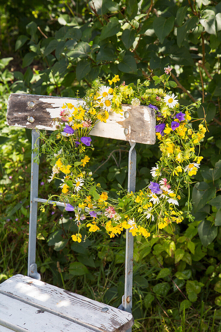 Blumenkranz aus Wildblumen auf rustikalem Gartenstuhl