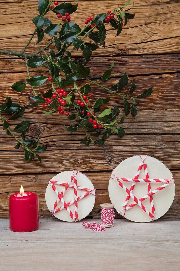 Weihnachtsdeko mit roter Kerze, Stechpalmenzweigen und runden Schachteln mit DIY-Sternen aus Strohhalmen