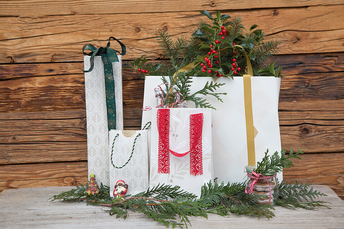 Christmas gift bags with fir branches in front of a wooden wall