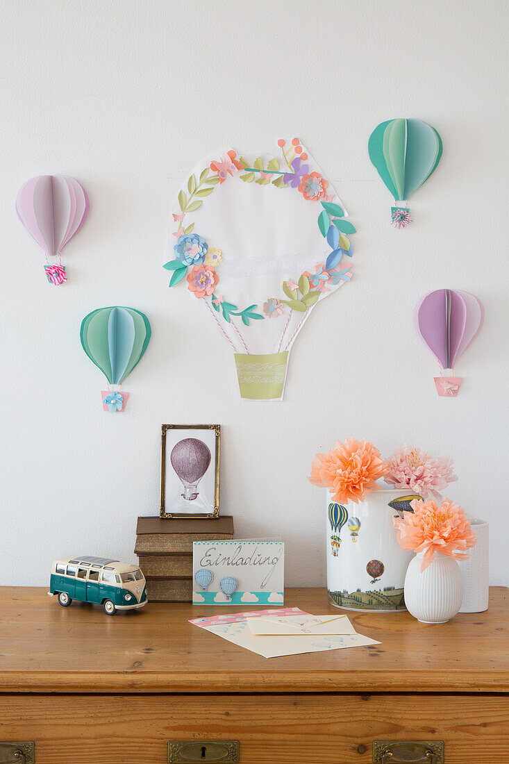 Hot air balloons made of paper as wall decoration and flower vases on a wooden chest of drawers