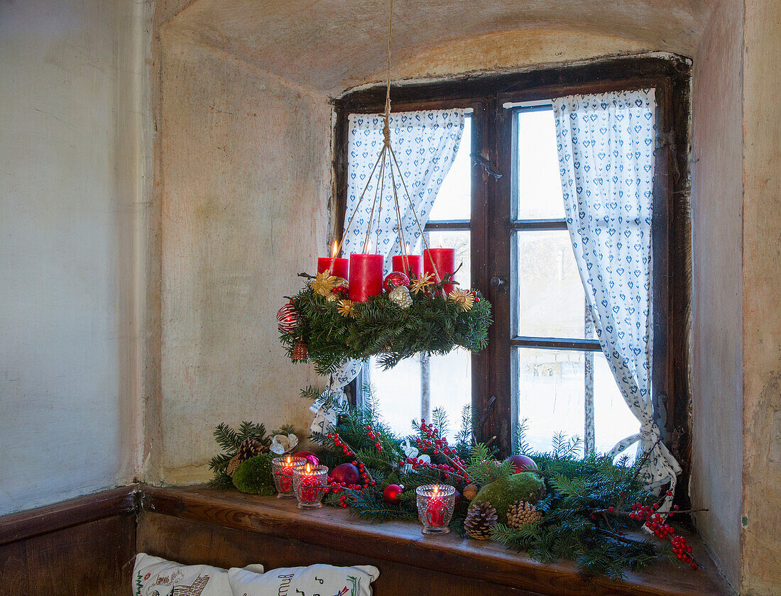 Hanging Advent wreath with red candles, below a Christmas decorated windowsill