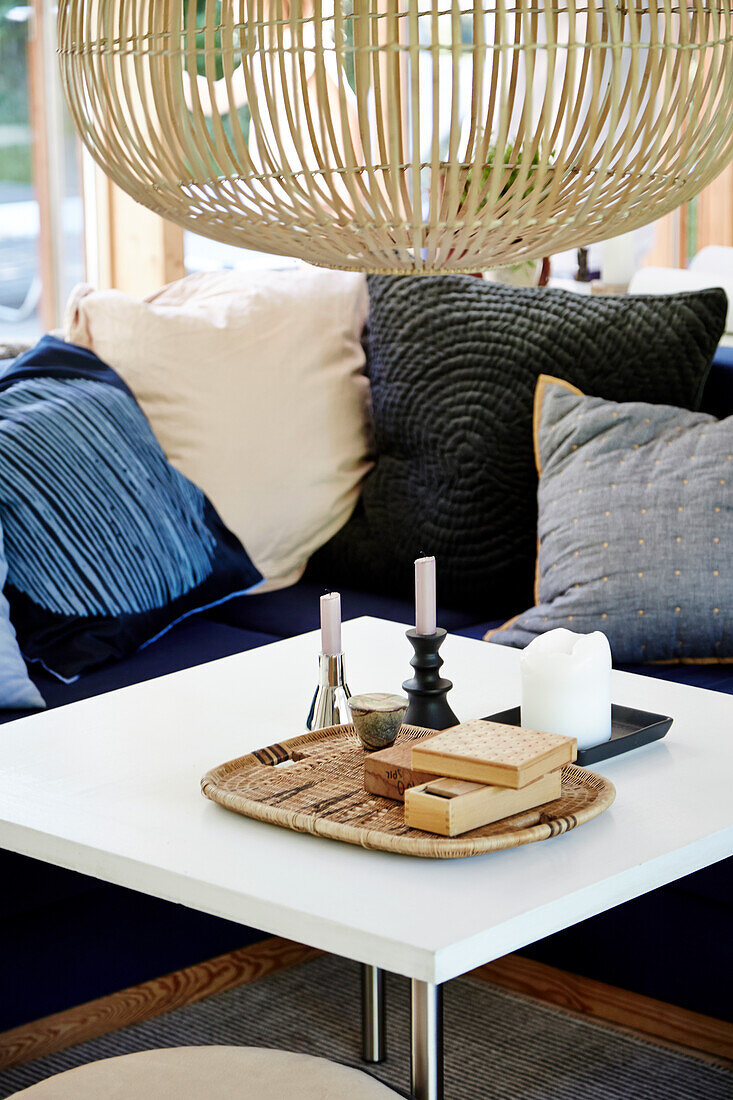 White coffee table with bamboo lamp above, pillow collection in the background