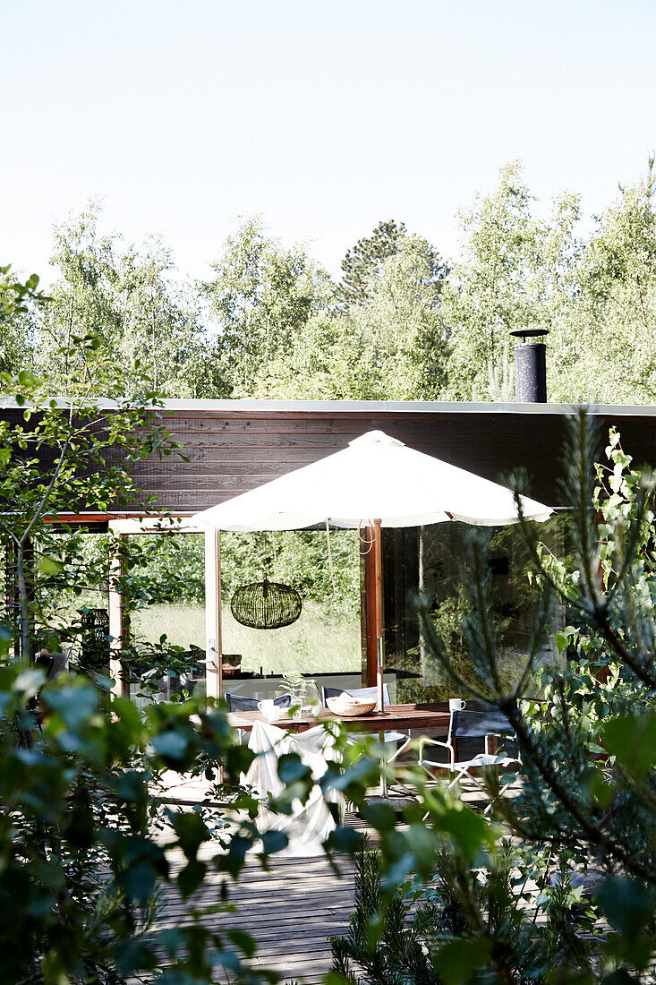 Tisch mit Stühlen und Sonnenschirm auf Holzterrasse