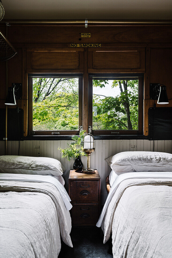 Two single beds and bedside table in old, rustic railway carriage