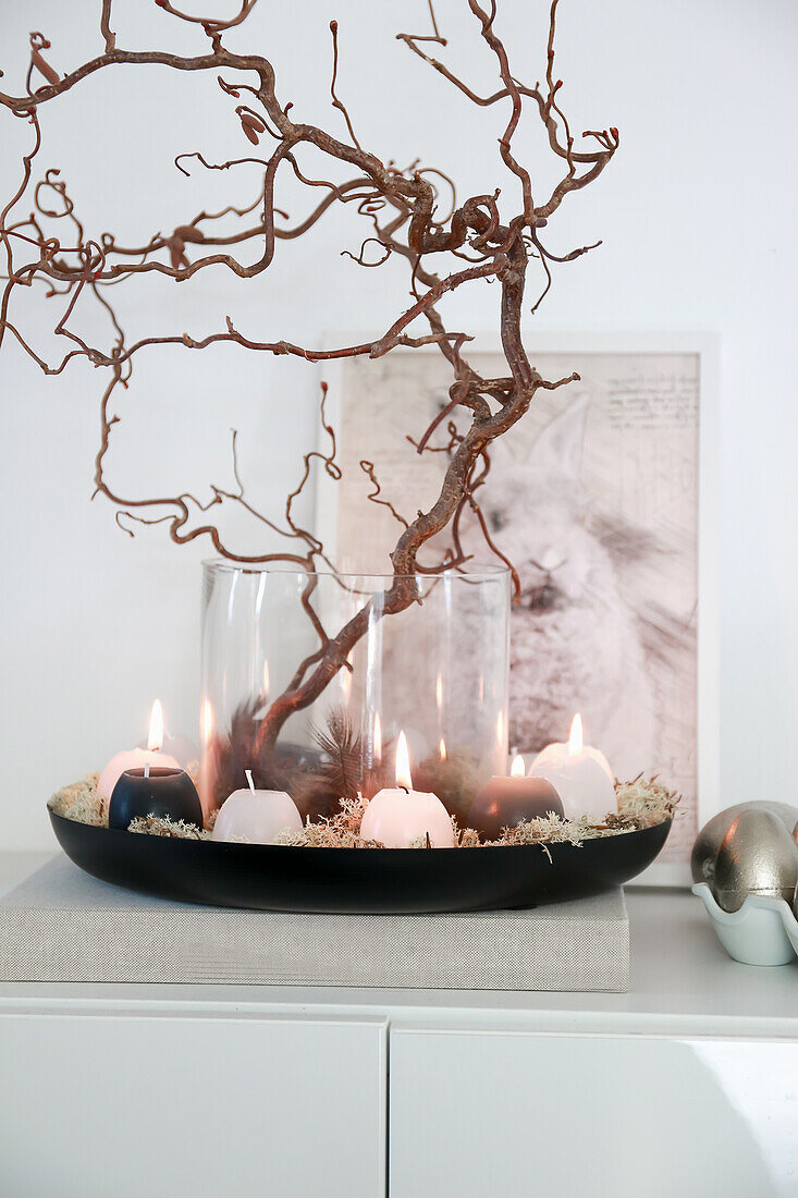 Decorative tray with candles and branches on sideboard, picture with bunny