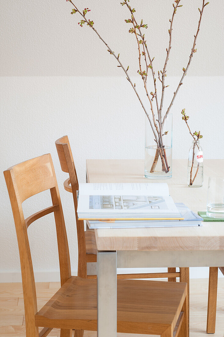 Book and vase of budding spring branches on pale table with chairs