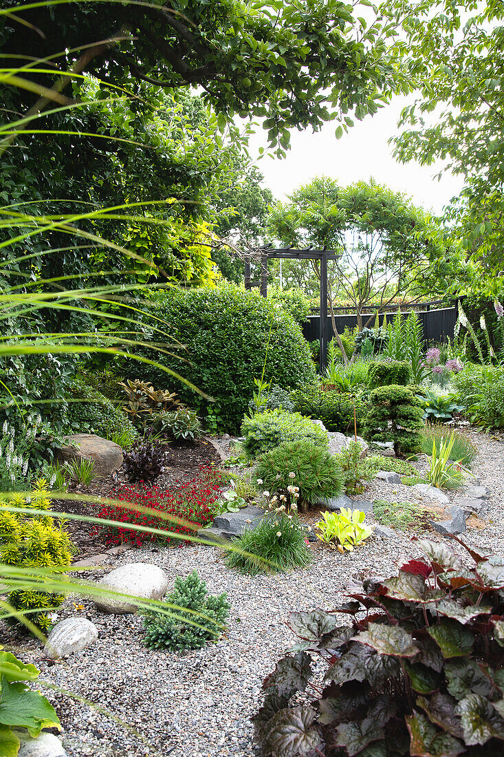 Gewundener Kiesweg durch gepflegten und vielfältig bepflanzten Garten