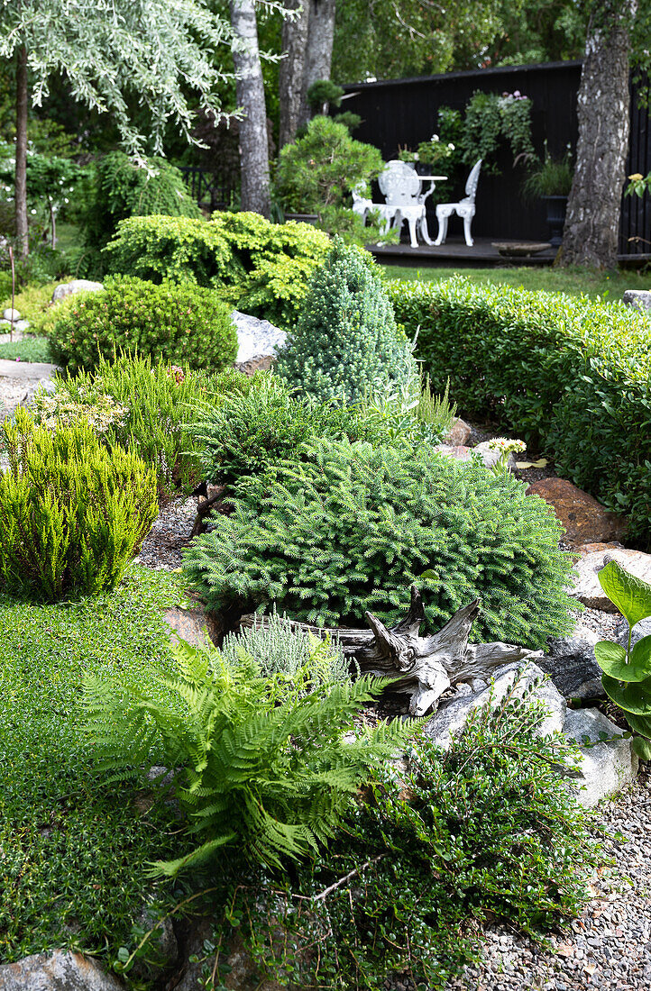 Vielseitig bepflanztes Gartenbeet mit weißer Gartenmöbel-Sitzgruppe im Hintergrund