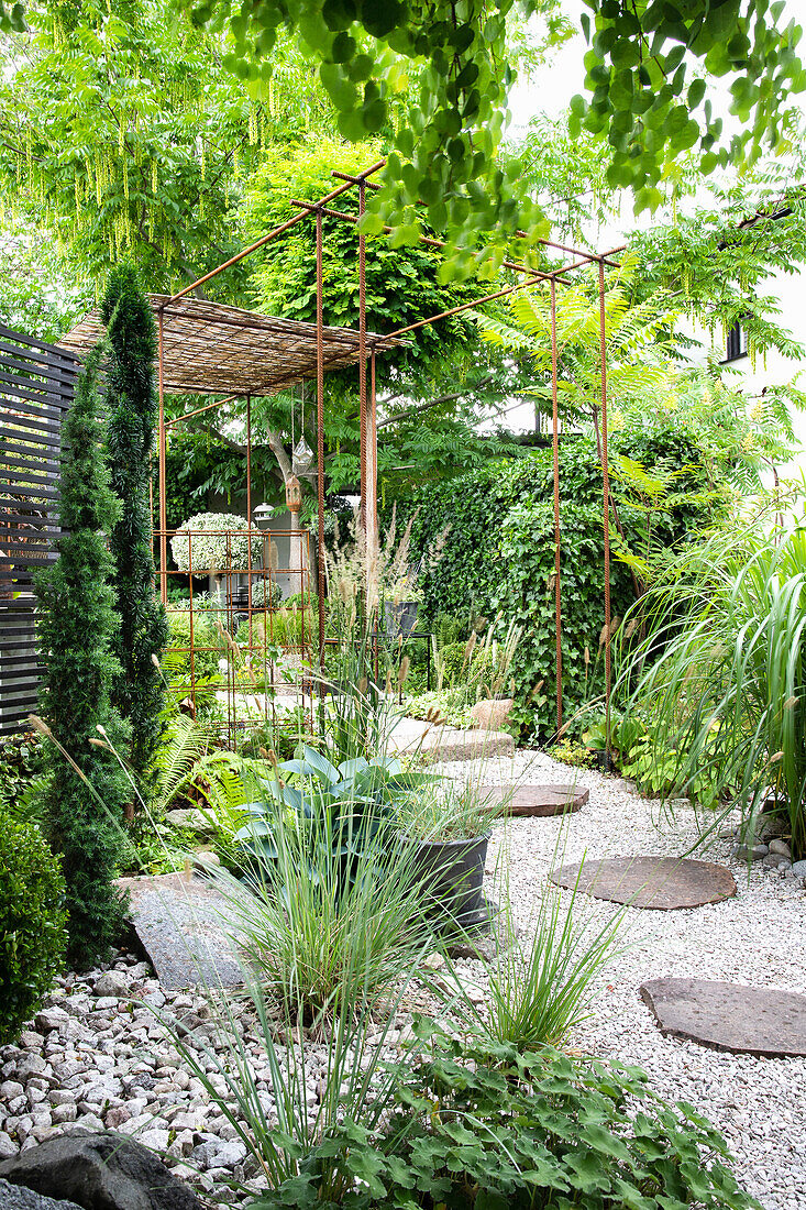 Kiesweg mit Trittplatten und bewachsene Pergola im Garten