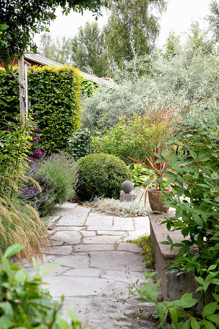 Steinweg durch vielfältig bepflanzten Garten mit Steinbank