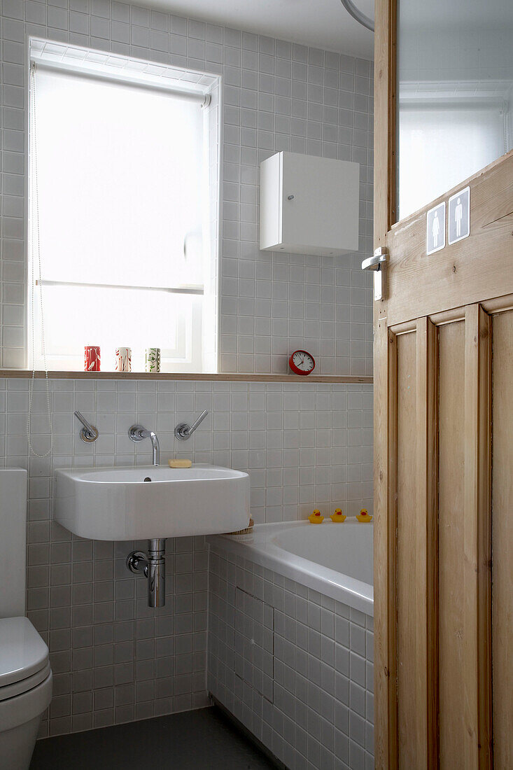 Kleines Badezimmer mit grauen Wandfliesen und gestreifter Holztür