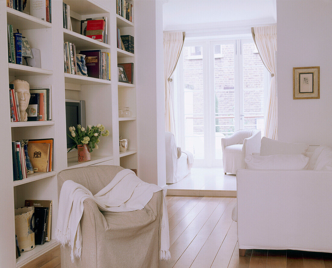 Ein traditionelles Wohnzimmer, dekoriert in neutralen Farben, gepolstertes Sofa, bedeckter Sitz, eingebaute Regale, gestrichene Dielen, Fenster