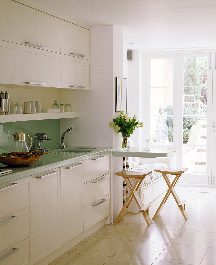 Moderne offene Küche in neutralen Farben mit Schränken und Spüle, Frühstücksbar, Hockern und gefliestem Boden