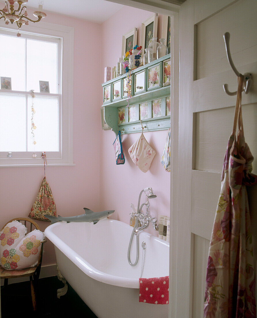 Ein traditionelles Badezimmer mit rosafarbenen Wänden und einem dekorativen grünen Schubladenset über einer gusseisernen Badewanne mit einem Spielzeug-Hai