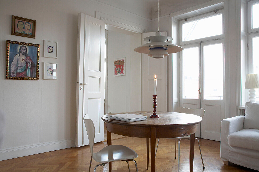 Lit candle on wooden table with pendant light and religious iconography in 20th century Stockholm apartment