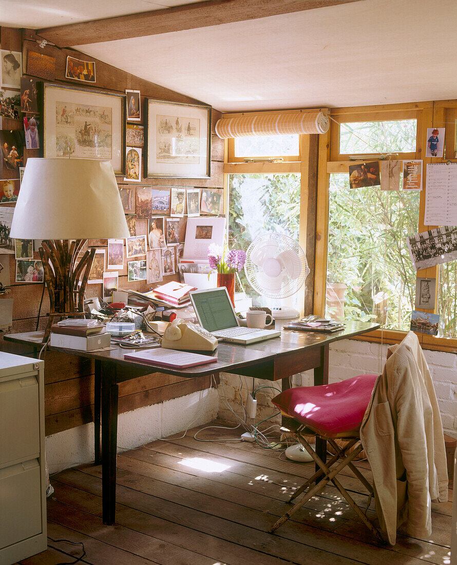 Ein traditionelles Büro mit einer Dachschräge und gerahmten Bildern neben einem Holzschreibtisch mit einem großen Lampenschirm und einem Telefon