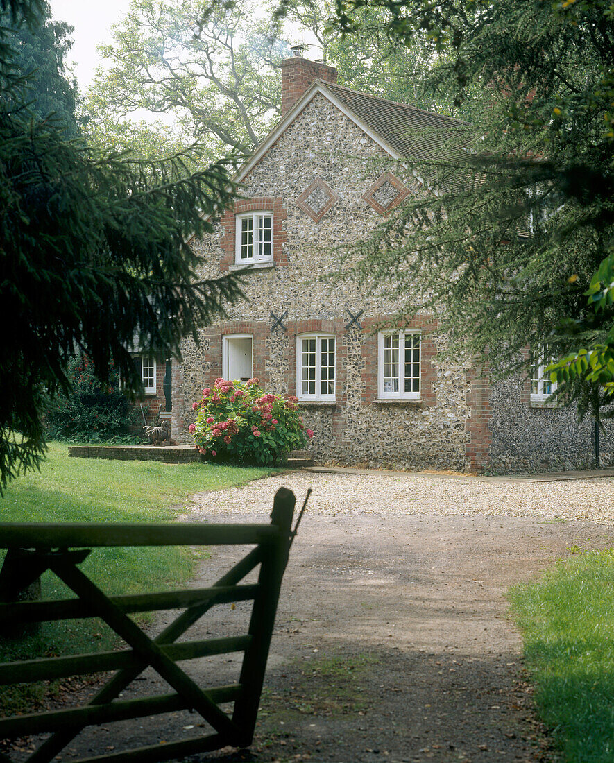 Außenansicht eines traditionellen Landhauses aus Backstein und Feuerstein, umgeben von Bäumen und Gras