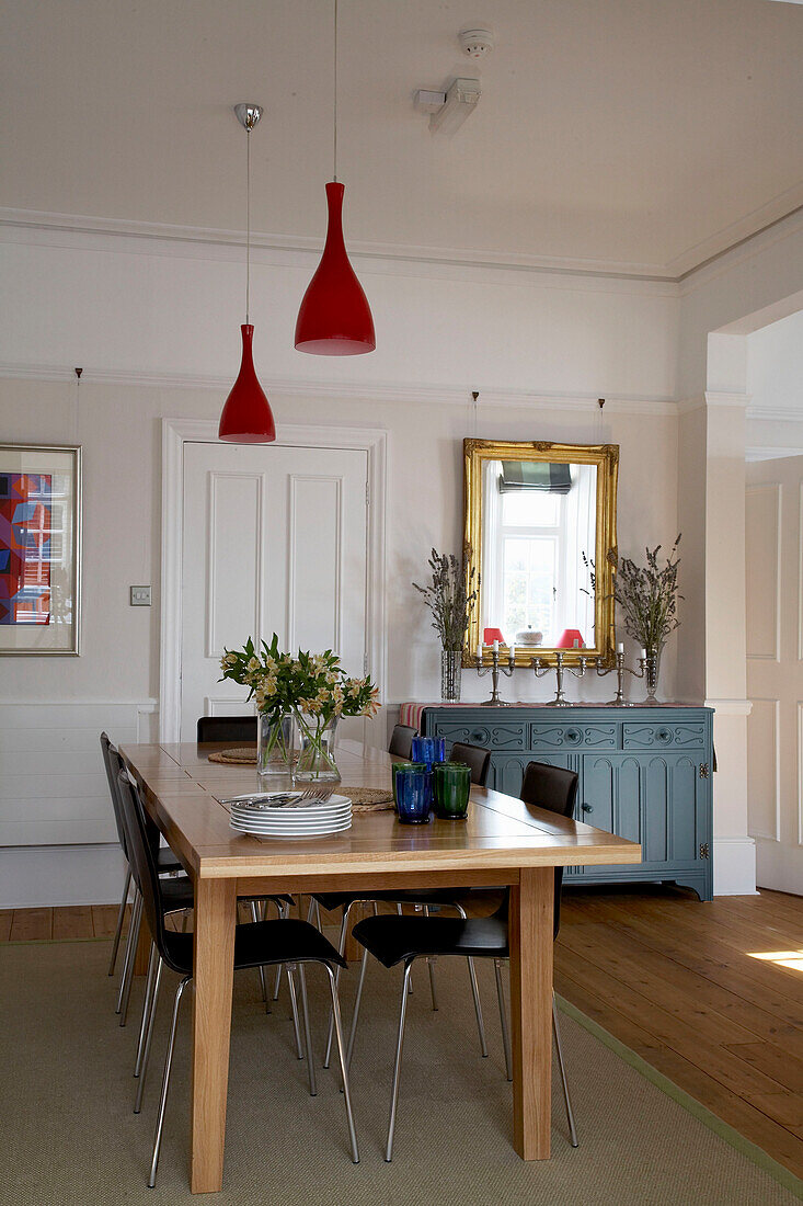 Esstisch aus Holz mit roten Hängelampen in einer Wohnung in Devon