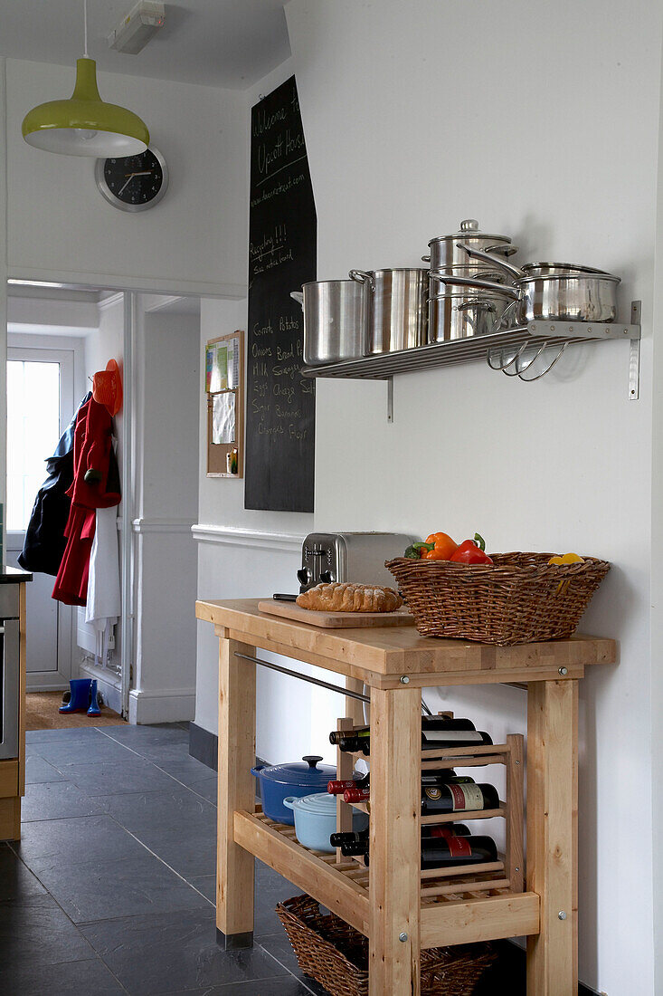 Coats hang in doorway of Devon kitchen with wooden butlers block under saucepans on metal shelf