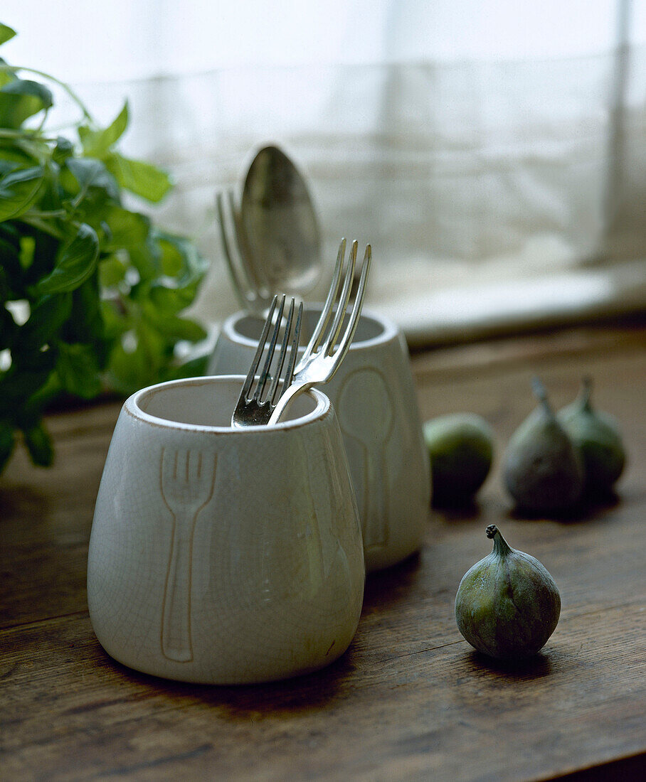 Ceramic pots with cutlery next to figs on window sill