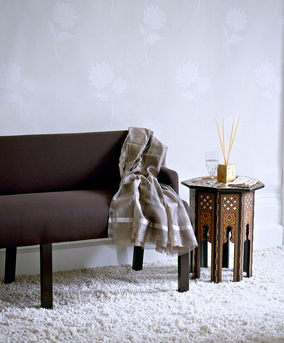 Braunes Sofa mit gestreifter Decke auf weißem Zottelteppich und marokkanisch geschnitztem Beistelltisch