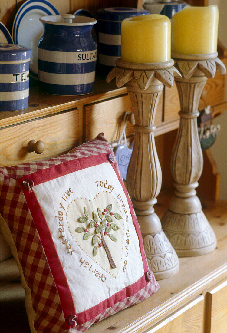 Close up detail of an embroidered cushion next to two large wooden candle holders on a pine dresser