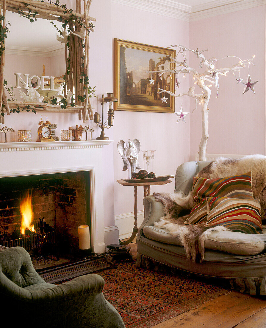 A traditional living room with a lit fireplace underneath an elaborately decorated mirror with a sofa and armchair in front