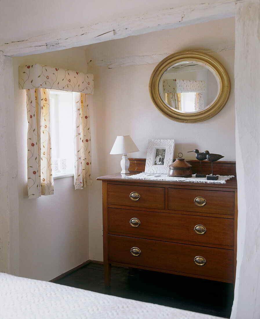Kommode, Lampe und gerahmtes Bild, darüber traditioneller runder Spiegel in Nische mit kleinem Fenster in Zimmer im Landhausstil