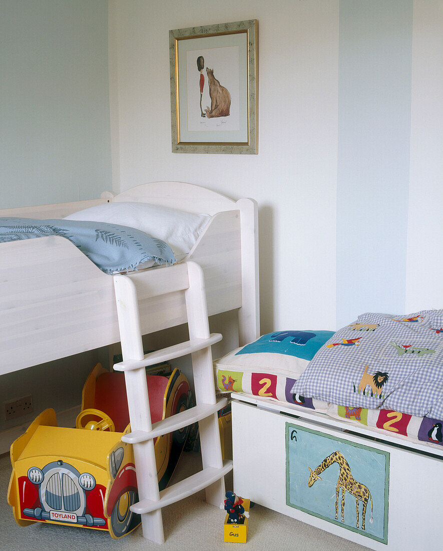 A traditional children's bedroom with a framed picture above a decorated storage chest next to a small ladder leading up to a bunk bed