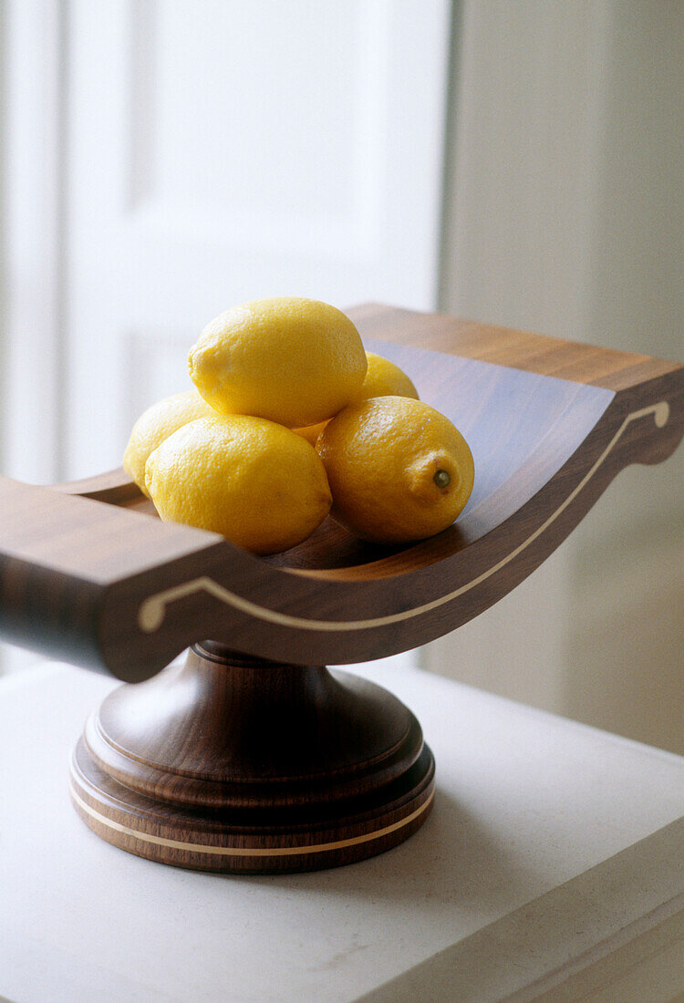 A detail of a wooden bowl of lemons on a window still