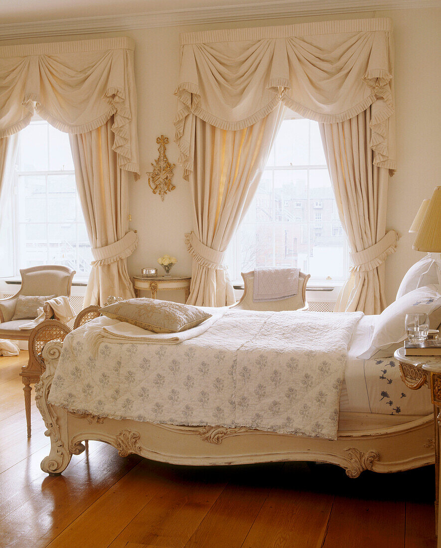 Ein traditionelles Schlafzimmer mit Holzfußboden, einem verzierten antiken Doppelbett, einem Fenster mit Gardinen und einem Sessel